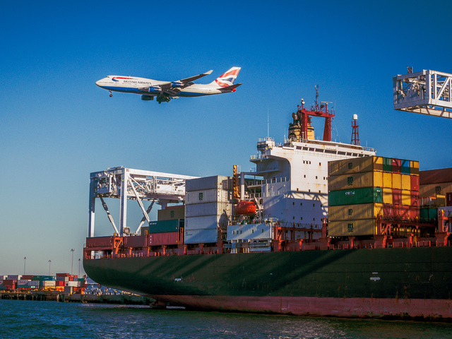 Ett flygplan passerar en hamn med lastfartyg.