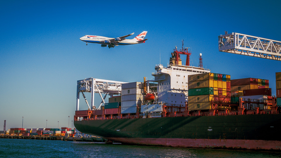 Ett flygplan passerar en hamn med lastfartyg.