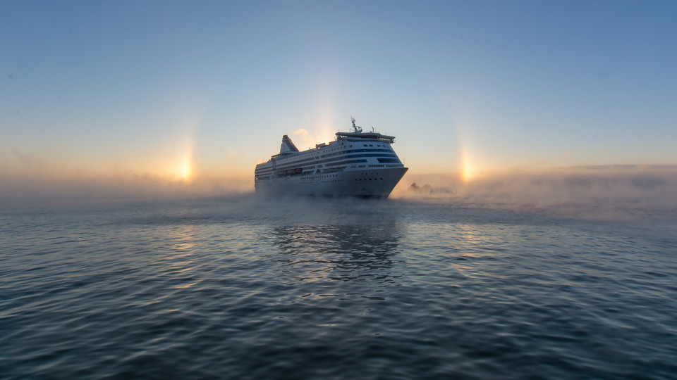 Ett stort fartyg färdas över Östersjön. med soluppgång i bakgrunden.
