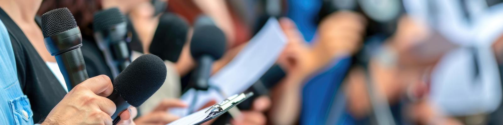 Journalister samlade under en presskonferens med anteckningsblock och mikrofoner,