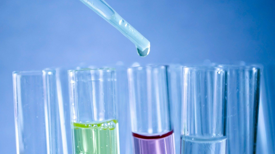 Test tubes being filled with coloured fluids by a pipette